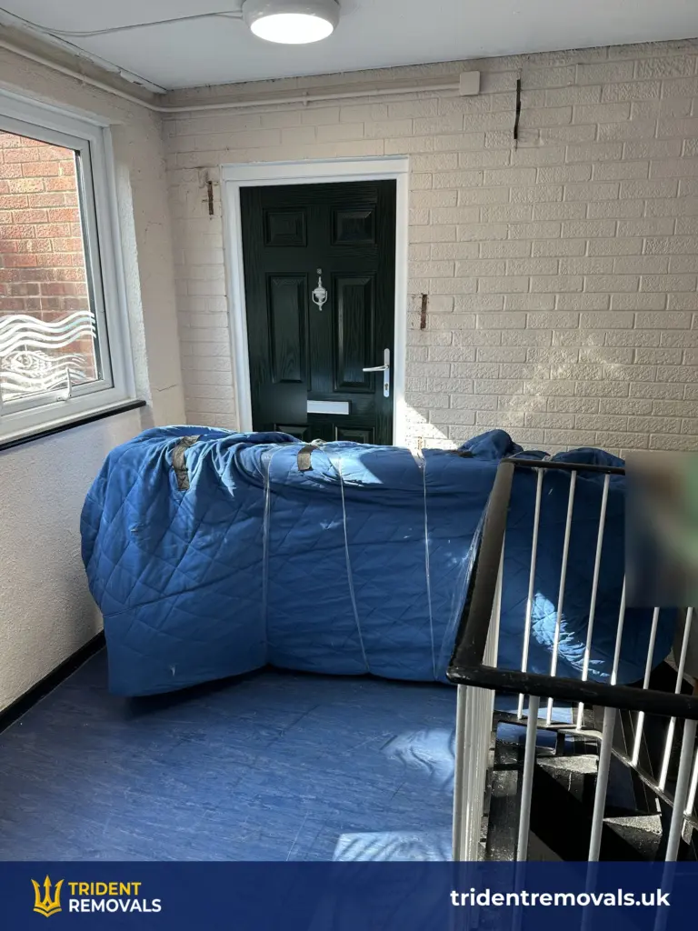 Wrapped sofa being carried down the stairwell during a Grovelands flat removal
